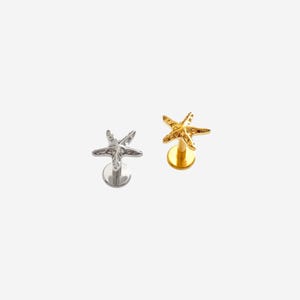 May include: Two body jewelry studs featuring a starfish design. One stud is silver-toned with a metallic finish, and the other is gold-toned with a metallic finish. Each piece has a flat circular base and a post extending to the starfish top.