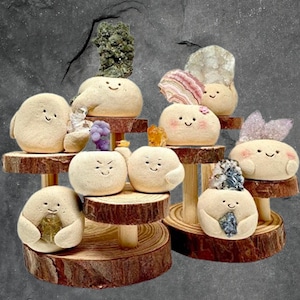 Puede incluir: Un conjunto de ocho pequeñas figuritas de cerámica con caras felices, cada una sosteniendo un cristal o piedra diferente. Las figuritas están dispuestas en tres niveles de madera.