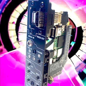 Può includere: Modulo elettronico nero con l'etichetta "VIDEO SLOOPER" con varie porte e pulsanti. Include testo come "MEDIA IN", "VIDEO OUT", "TRIG IN" e "RAZMASYNTH". Il modulo ha un complesso circuito stampato visibile.