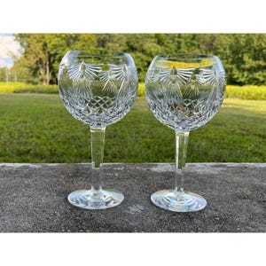 Peut inclure: Deux verres à vin en cristal transparent avec des motifs gravés complexes. Les verres ont une forme de bol rond, de longues tiges et des bases circulaires. Le motif gravé comprend des losanges et des motifs stylisés en forme d'ailes, créant une apparence décorative et élégante.