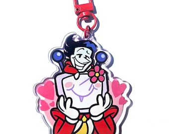 May include: A cartoon character keychain with a red clasp. The character has a white face, black hair, and is wearing a red outfit. The keychain has a pink heart background and a pink flower.