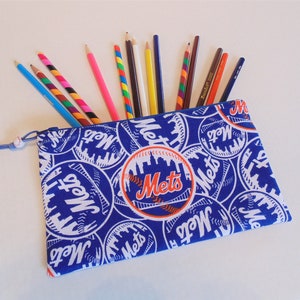 May include: A blue pencil case with a zipper closure and a repeating pattern of white baseballs with the word "Mets" in orange and blue. The case is filled with colored pencils.
