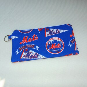 May include: A blue zippered pouch with a white zipper. The pouch is decorated with a repeating pattern of the New York Mets logo, including the team name and a baseball with the city skyline.