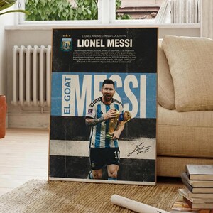 Peut inclure: Une affiche encadrée représentant Lionel Messi tenant un trophée, avec le texte "EL GOAT" et "MESSI". L'affiche comprend un texte biographique et la signature du joueur. La palette de couleurs est noire, blanche et bleue.