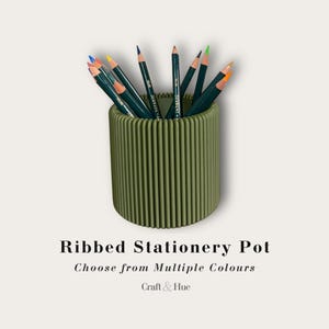 May include: A cylindrical olive green stationery pot with a vertical ribbed texture, filled with an assortment of coloured pencils. The text below reads: Ribbed Stationery Pot, Choose from Multiple Colours, Craft & Hue.