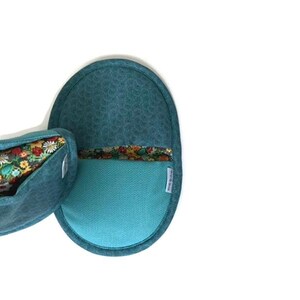 May include: Two teal oven mitts. One mitt is oval-shaped with a floral pattern on the inside and a teal exterior. The other mitt is a matching oval shape with a teal exterior and a floral pattern on the inside. The mitts are made of fabric.