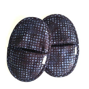 May include: A pair of dark blue oven mitts with a white polka dot pattern. The mitts are oval shaped and have a white fabric lining.