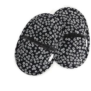 May include: A pair of oval-shaped fabric slippers featuring a black background with a repeating white floral pattern. Each slipper has a horizontal black and white striped elastic band across the top and a small white fabric tag on the side.
