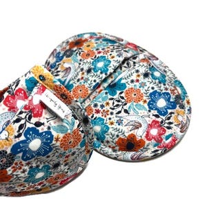 May include: Floral-patterned bra with red, blue, and orange flowers on a white background. The bra features a colorful design with a mix of flowers and birds. The tag reads "Simply Yours".