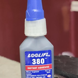 Puede incluir: Una botella gris de adhesivo instantáneo LOOLIFL 380 con una tapa azul. La etiqueta dice "Black Toughened 200cP", "PALT NO 38050", "REFRIGERATE FOA STORAGE", "SHAKE WELL BEFORE USE", "MT20241208 BY 20261207", "NET WT. 1 OZ (20g)".