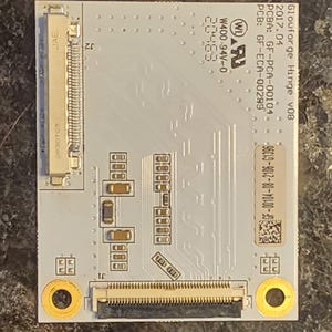 May include: A rectangular circuit board with the text "Glowforge Hinge V08" and other technical details. The board is light gray with various electronic components, connectors, and gold-colored circular elements. The image is a top-down view.
