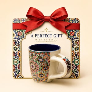 Peut inclure: Un mug en céramique avec un motif mosaïque géométrique coloré et un intérieur bleu foncé, placé devant une boîte cadeau carrée avec une bordure mosaïque assortie, un centre crème et un grand nœud en satin rouge sur le dessus.