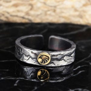Op de afbeelding: Een zilveren ring met een getextureerd oppervlak en een gouden adelaar kop ontwerp.