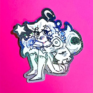 Pode incluir: Um autocolante holográfico com uma personagem de desenho animado com olhos grandes, uma estrela e uma lua crescente. A personagem é branca com detalhes azuis, num fundo rosa brilhante. O autocolante tem uma borda brilhante.