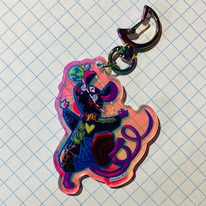 May include: A colorful acrylic keychain featuring a stylized rat design. The rat is primarily black and blue, with pink, yellow, and green accents. It has a rainbow-colored clasp and the text "OHHACR-D".