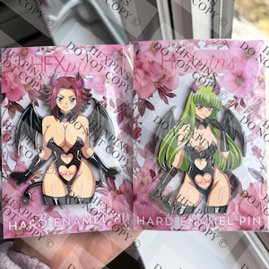 Może przedstawiać: Dwie emaliowane przypinki w stylu anime przedstawiające żeńskie postacie ze skrzydłami i wzorami w kształcie serca. Jedna przypinka ma postać o rudych włosach, druga o zielonych włosach. Przypinki są zapakowane na różowych kwiatowych tłach.