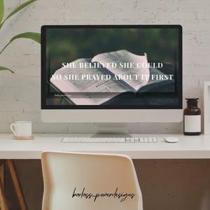 May include: A desktop computer displays the text "SHE BELIEVED SHE COULD SO SHE PRAYED ABOUT IT FIRST" over an open book. The computer sits on a white desk with a white chair, a coffee cup, and a decorative bottle.