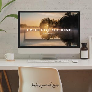 May include: A desktop computer shows a tranquil landscape with the words "I WILL GIVE YOU REST Matthew 11:28". The image includes a lake, trees, and a sunset. A white desk supports the computer, a cup, a bottle, and a chair.