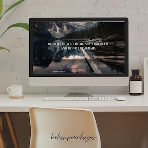 Peut inclure: Un écran d'ordinateur affiche une image de lac avec le texte "DO NOT LET YOUR HEARTS BE TROUBLED AND DO NOT BE AFRAID." Un bureau blanc avec une tasse, un clavier et une souris. Une bouteille marron et une plante sont également visibles.