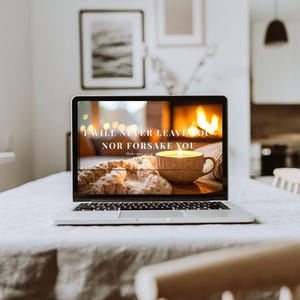 May include: A laptop screen shows a warm scene with a lit candle in a mug, a knitted blanket, and a fireplace. The text on the screen reads "I WILL NEVER LEAVE YOU NOR FORSAKE YOU" with a Bible verse reference. The laptop is on a white tablecloth.