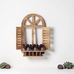 Op de afbeelding: Houten raamkozijn met open luiken en een kleine bloembak gevuld met paarse bloemen. Het raam is op een witte muur gemonteerd. Verschillende kleine vetplanten zijn eronder geplaatst.