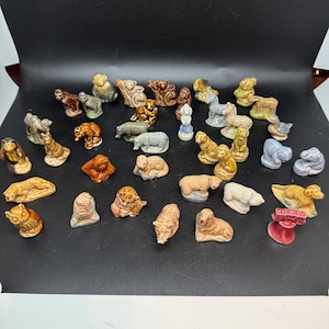 May include: A selection of small ceramic animal figurines. The figurines depict various animals, including bears, monkeys, and rhinos, in shades of brown, tan, and grey. Some are standing, others are lying down. The collection is diverse.