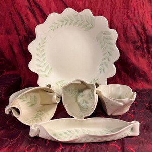 May include: A collection of off-white ceramic serving dishes with a delicate green leaf pattern. The set includes a large scalloped-edge platter, a long rectangular dish, and three smaller bowls, perfect for serving appetizers or desserts.