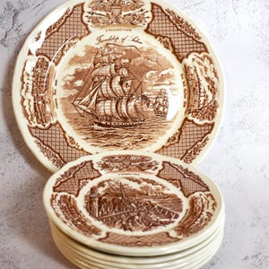 Puede incluir: Una pila de ocho platos de cerámica marrón y blanco con un tema náutico. El plato superior presenta una ilustración marrón de un barco llamado "Friendship of Salem" con el texto "A Pilgrim Ship" y "Friendship of Salem".