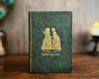 May include: A vintage green book titled "Etiquette for Ladies" with gold lettering and illustrations. The cover features two figures in period dress. The book is displayed on a wooden surface, suggesting a focus on historical or literary themes.