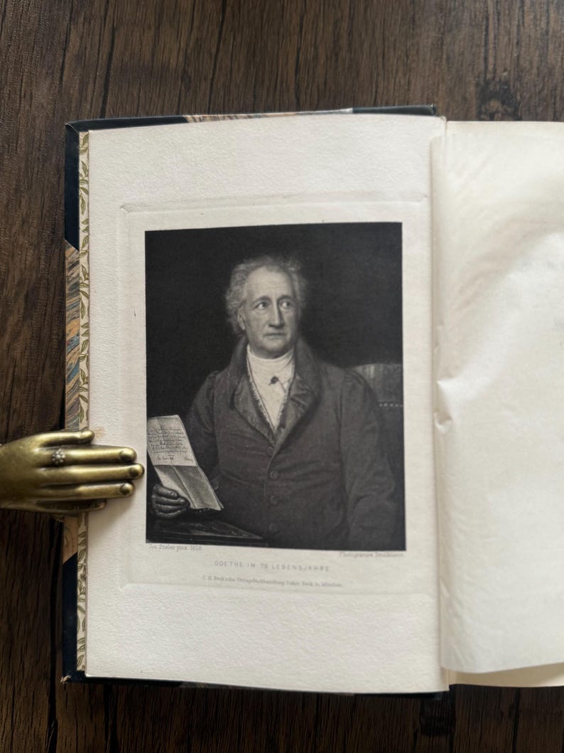 Puede incluir: Un libro abierto con un retrato en blanco y negro de un hombre sosteniendo un papel. El retrato est&aacute; enmarcado dentro de las p&aacute;ginas del libro. La columna del libro tiene un dise&ntilde;o.