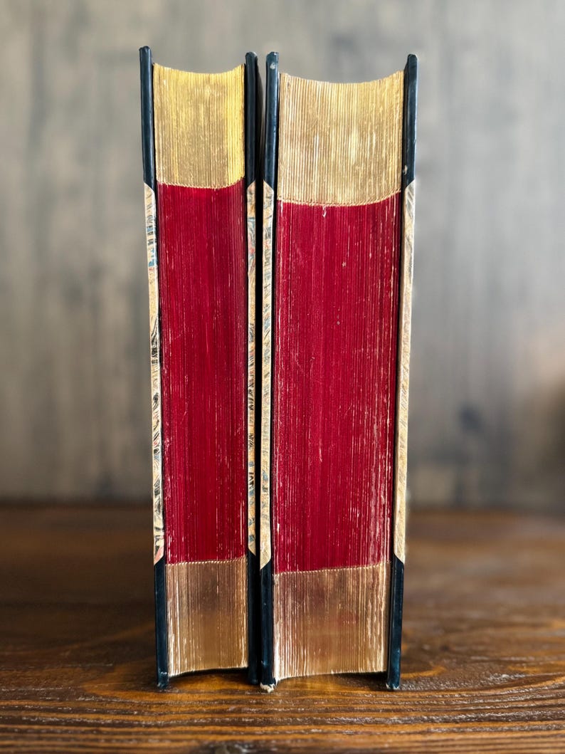 Puede incluir: Dos libros antiguos con cubiertas rojas y bordes dorados. Las espinas son negras y las p&aacute;ginas son de color rojo intenso. Los bordes superior e inferior de las p&aacute;ginas son dorados, creando un contraste llamativo. Los libros est&aacute;n de pie.