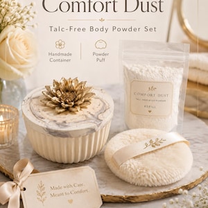 Puede incluir: Un set de polvos corporales sin talco Comfort Dust que incluye un recipiente redondo acanalado con tapa de flor dorada, una bolsa de recarga de polvo blanco y una borla color crema con cinta. Una etiqueta dice, Made with Care. Meant to Comfort.