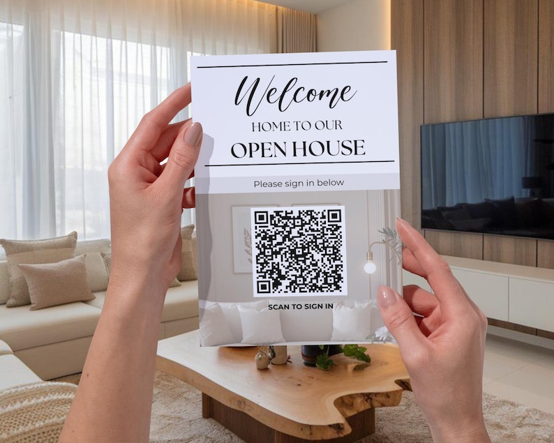 May include: A sign that reads "Welcome Home to Our Open House" is held up in front of a living room. The sign has a QR code and the words "Scan to Sign In" below it. The sign is white with black text.