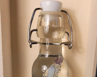 May include: A small glass bottle with a metal clasp closure filled with clear liquid and blue and purple stones.