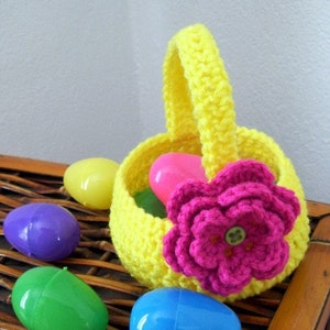 May include: A yellow crocheted Easter basket with a pink crocheted flower and a button in the center. The basket is filled with plastic Easter eggs in various colors, including purple, green, blue, and yellow.