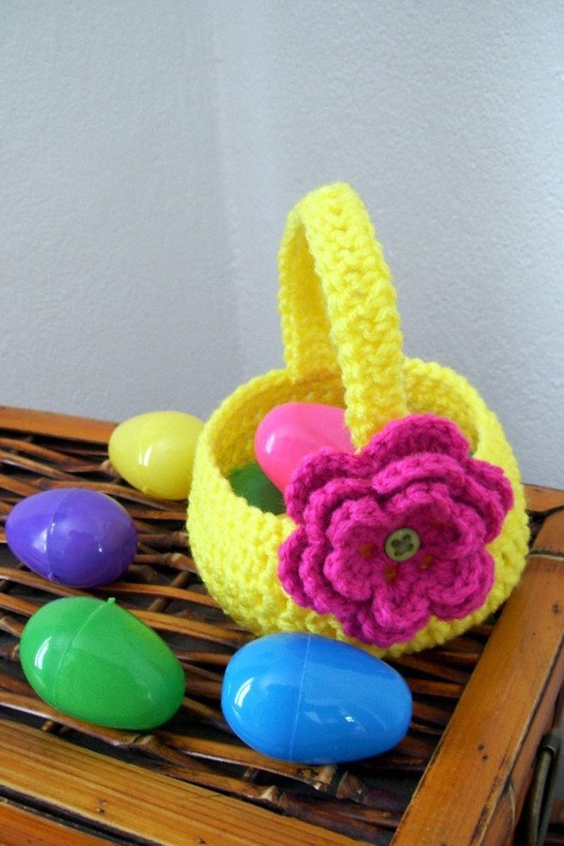 May include: A yellow crocheted Easter basket with a pink crocheted flower and a button in the center. The basket is filled with plastic Easter eggs in various colors, including purple, green, blue, and yellow.