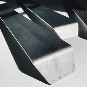 May include: Three silver metal pieces with a sharp, angled edge. The pieces are arranged in a triangular shape.