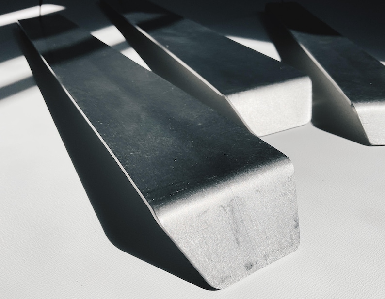 May include: Three silver metal pieces with a sharp, angled edge. The pieces are arranged in a triangular shape.