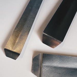 May include: Three metal strips with different finishes. The strip on the left is a light gold color, the strip in the center is dark gray, and the strip on the right is black.