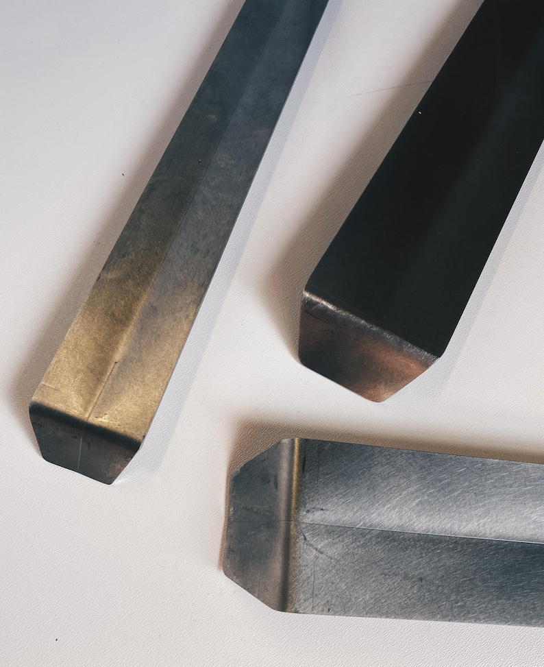 May include: Three metal strips with different finishes. The strip on the left is a light gold color, the strip in the center is dark gray, and the strip on the right is black.