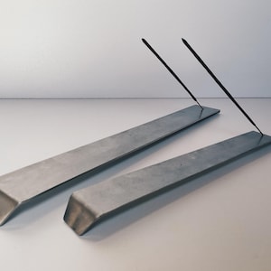 May include: Two silver metal incense holders with two black incense sticks resting on top.