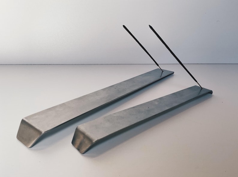 May include: Two silver metal incense holders with two black incense sticks resting on top.
