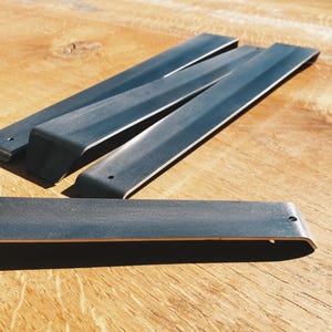 May include: Four black metal shelf brackets with rounded edges and a single hole on each bracket.