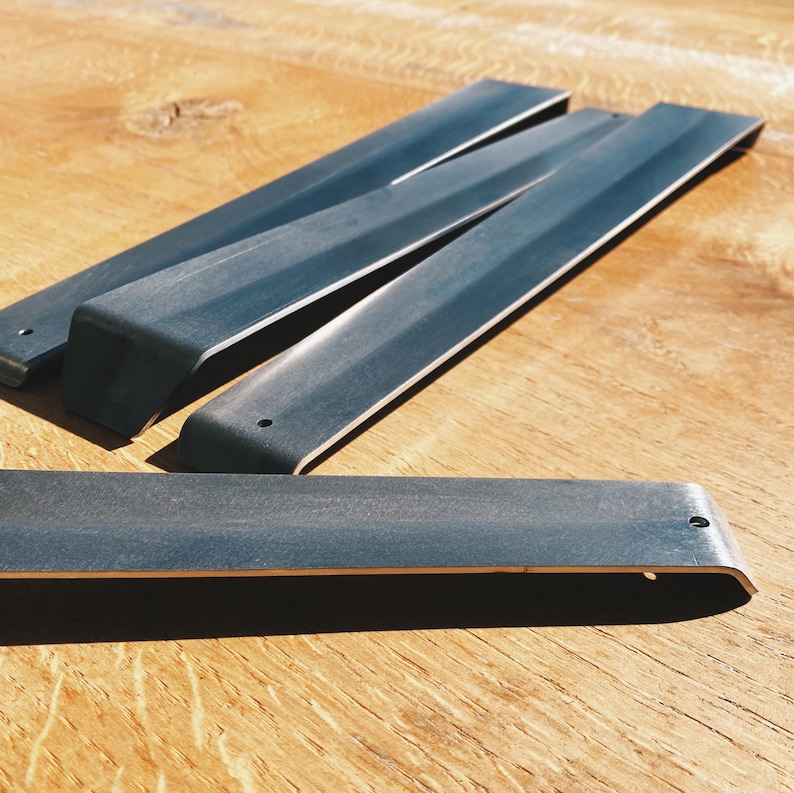 May include: Four black metal shelf brackets with rounded edges and a single hole on each bracket.