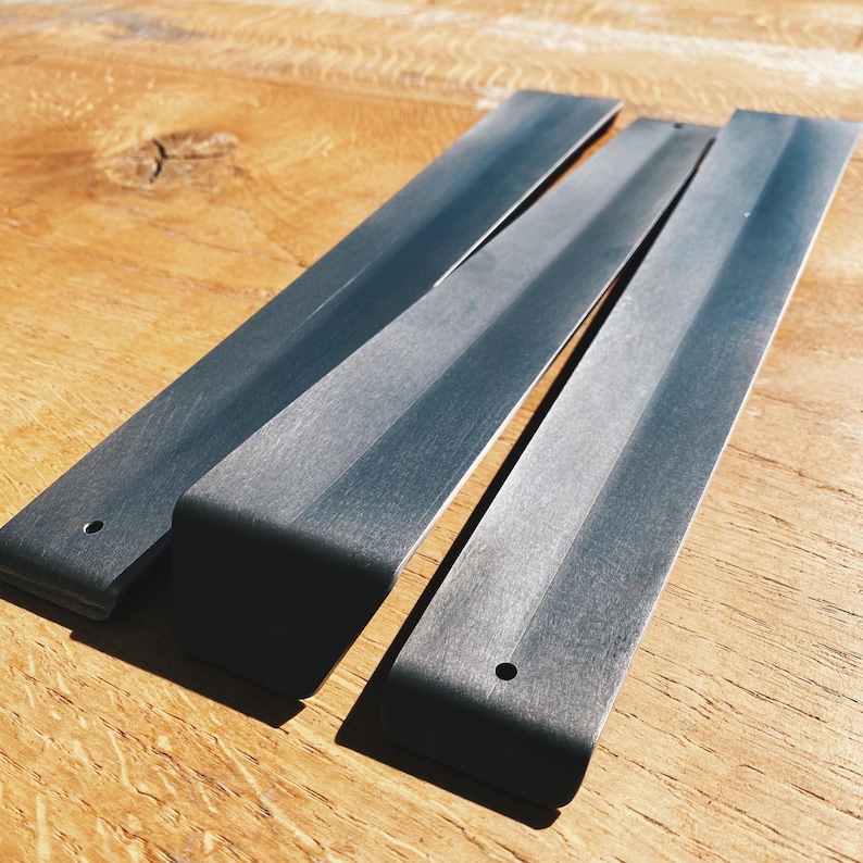 May include: Three black metal incense sticks with rounded edges and a hole in the center. The sticks are stacked on top of each other on a wooden surface.
