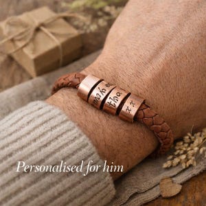 May include: A brown leather bracelet with copper-coloured cylindrical beads. Each bead is engraved with a name. The bracelet is braided and worn on a wrist. The text "Personalised for him" is at the bottom of the image.
