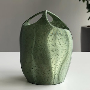 May include: A green vase with a textured surface and two arched handles. The vase has a metallic sheen and a unique, organic pattern. The vase is likely used for decorative purposes.
