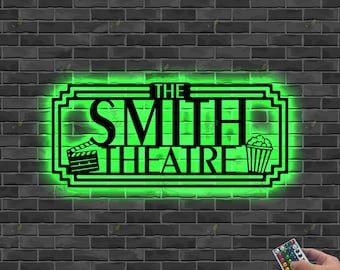 May include: Black metal sign with the text "THE SMITH THEATRE" in a green neon glow. The sign includes a film clapper and popcorn bucket. A hand holds a remote control with colorful buttons.