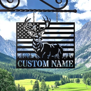 May include: A black metal sign featuring a deer silhouette against an American flag design. The sign includes the text "CUSTOM NAME" in a blue font, hanging from a decorative bracket.