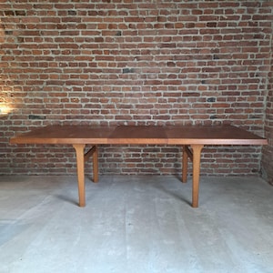 Puede incluir: Una mesa de comedor rectangular de madera larga con un acabado marrón claro. La mesa tiene un diseño sencillo con cuatro patas y una superficie lisa. La mesa mide aproximadamente 183 cm de largo.
